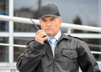Male security guard using portable radio outdoors Male security guard using portable radio outdoors
